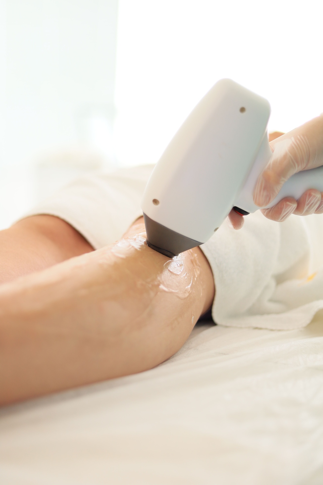 A qualified aesthetician at Vale Laser Aesthetics performing a diode laser hair removal treatment on a client's lower leg, with cooling gel applied to protect sensitive skin